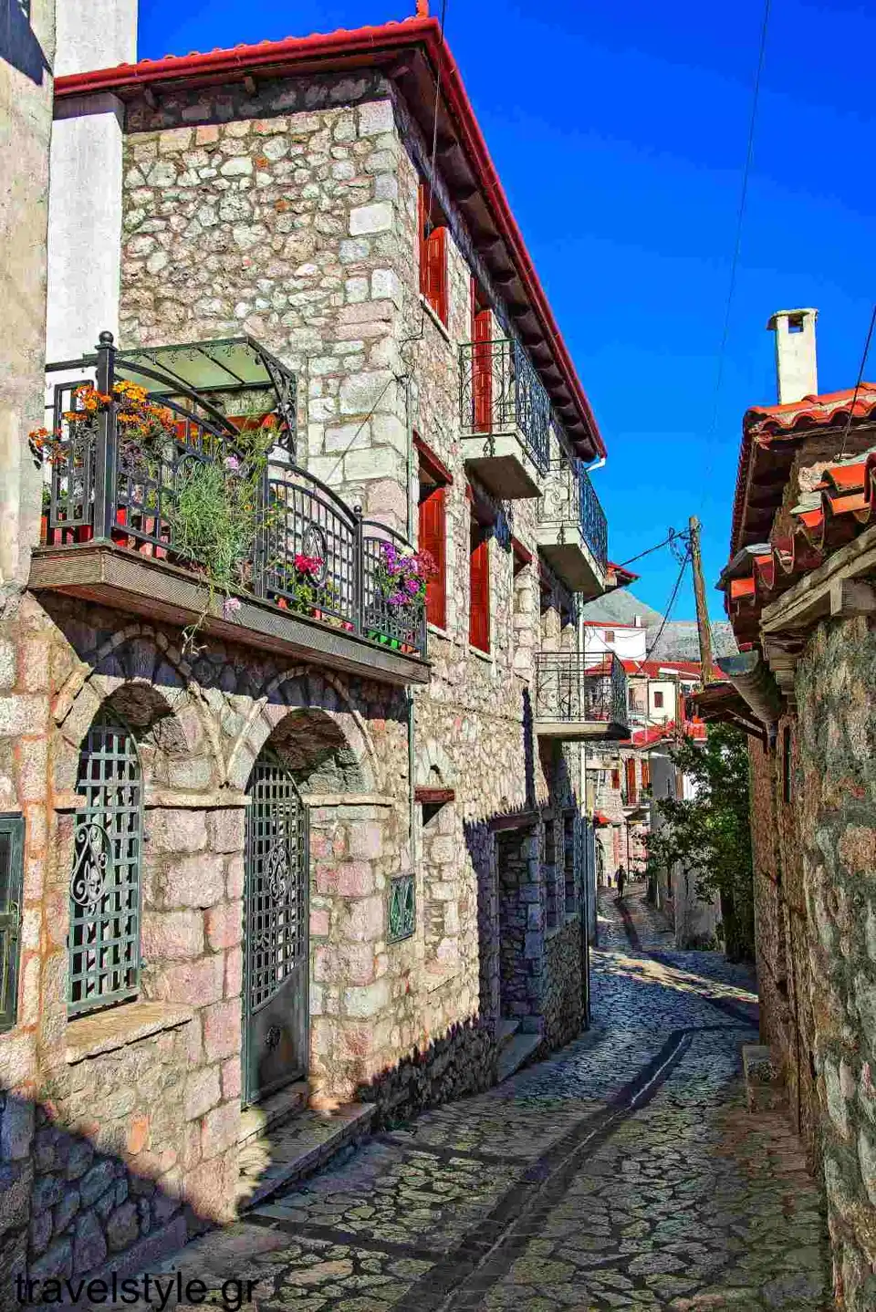 Πλακόστρωτο σοκάκι με πέτρινα σπίτια και κεραμοσκεπές στην Αράχωβα